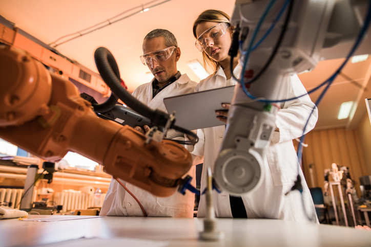 Low angle view of two engineers working on robotic arm in laboratory. Woman is using digital tablet.