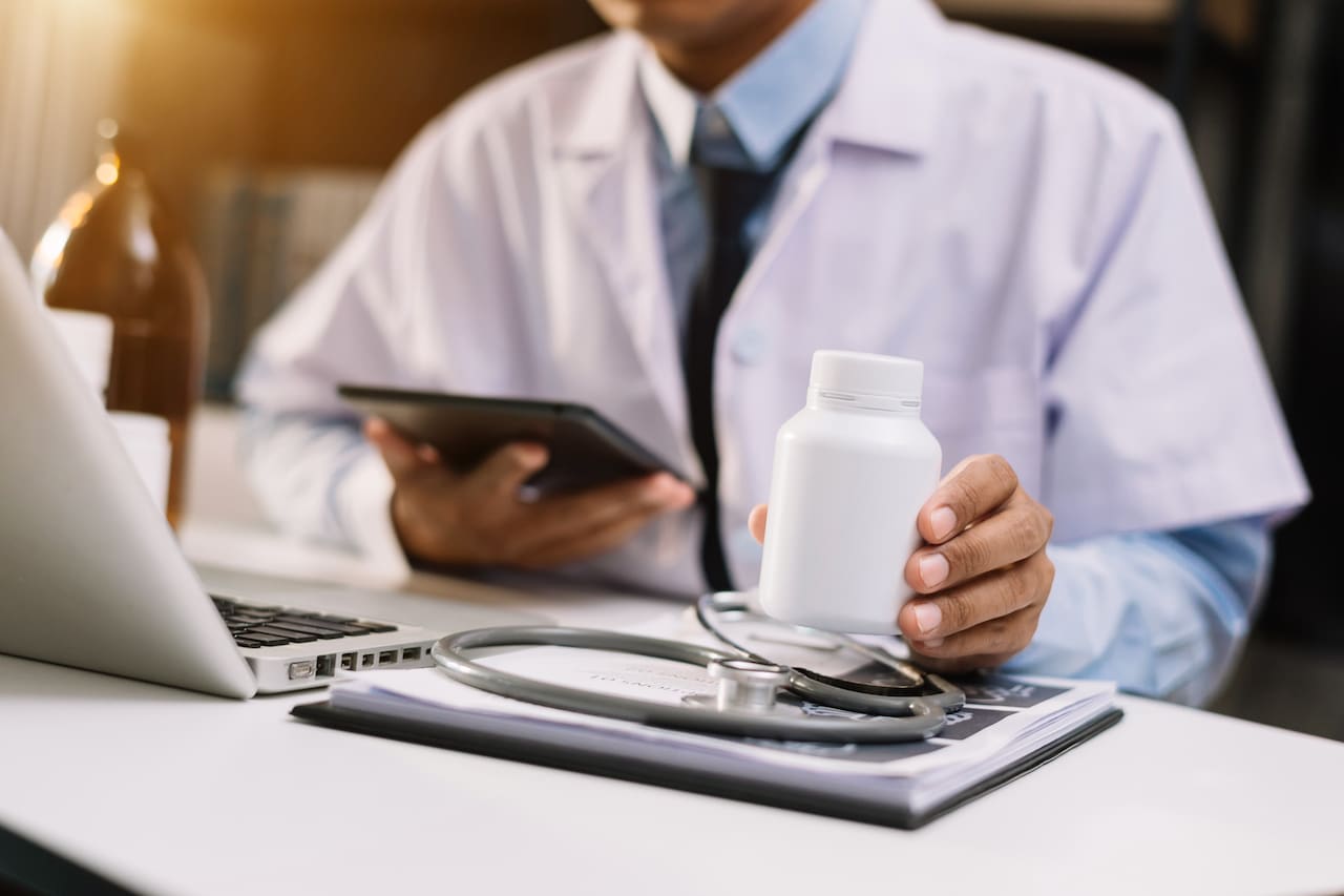 Doctor using laptop and holding medicine.