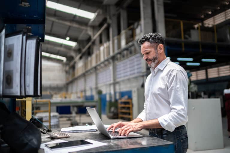 photo of white presenting man looking at a grey laptop with stacked shelves behind