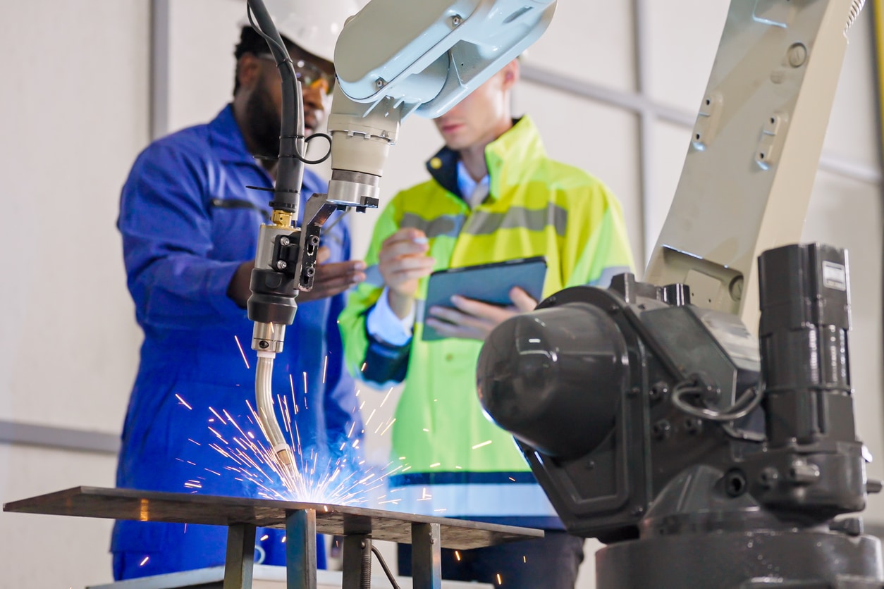 Nahaufnahme eines automatischen Schweißbrenners mit einem multiethnischen Ingenieurkollegen, der über das Roboterentwicklungswerk, die intelligente Fabrik und das Konzept der Industrie-Ingenieurintelligenz-Innovationstechnologie diskutiert